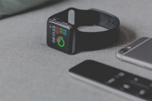 A black Apple Watch lays on the counter top, displaying a fitness tracking app, next to an iPhone