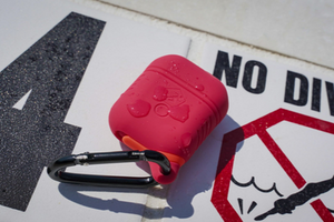 A red, water proof, Airpod case cover lays on a in-ground pool sign that says, 
