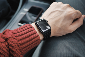 Guy sit in the passenger side of a car, with his hand on his leg. On his wrist is an Apple Watch.