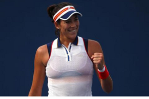 Garbiñe Muguruza wears a hat and wrist band with her hand clinched and a smile. She's excited.